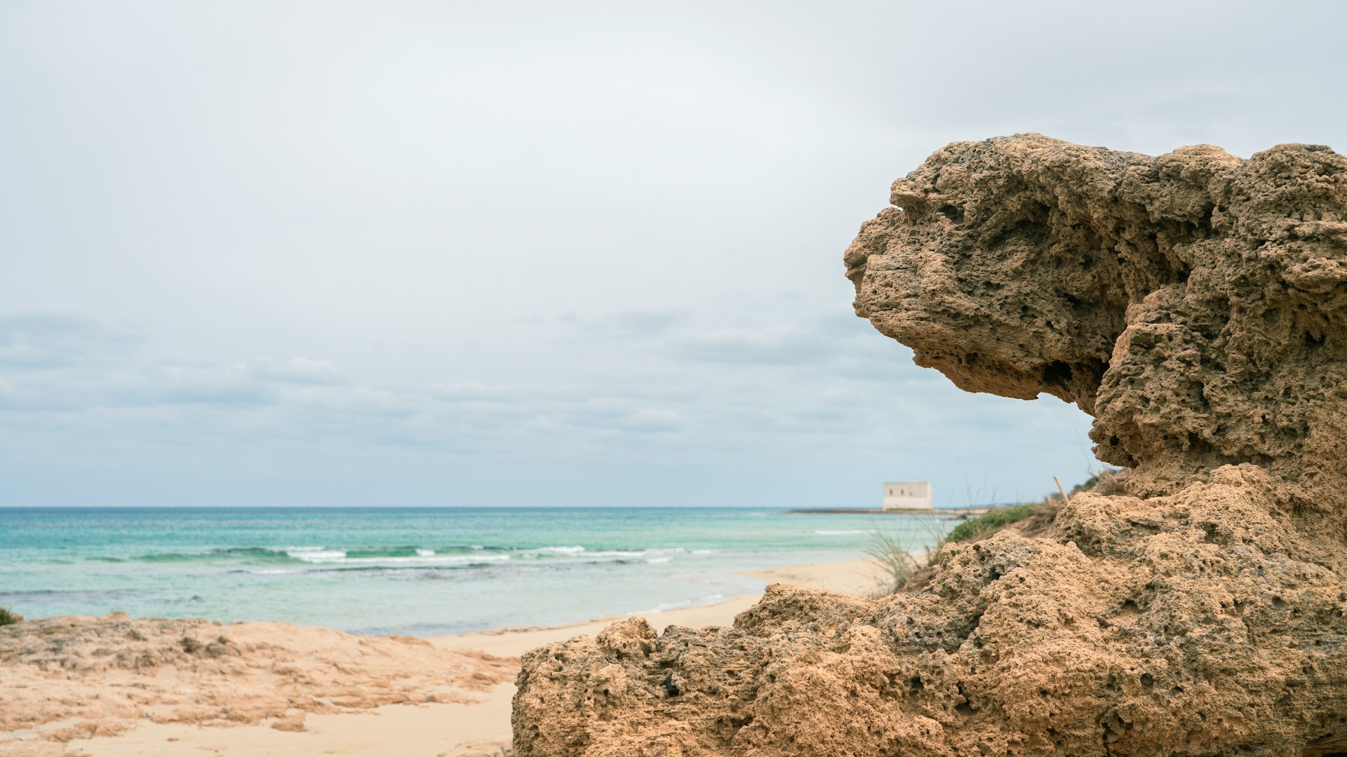 Rocky foreground overlooks a serene beach and ocean.