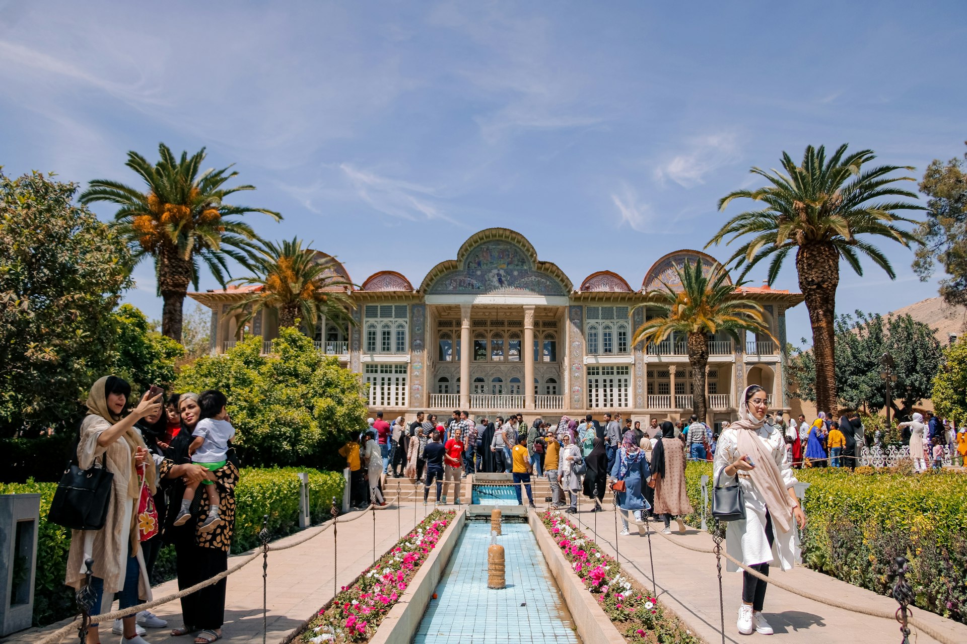 a group of people walking on a walkway in front of Eram Garden