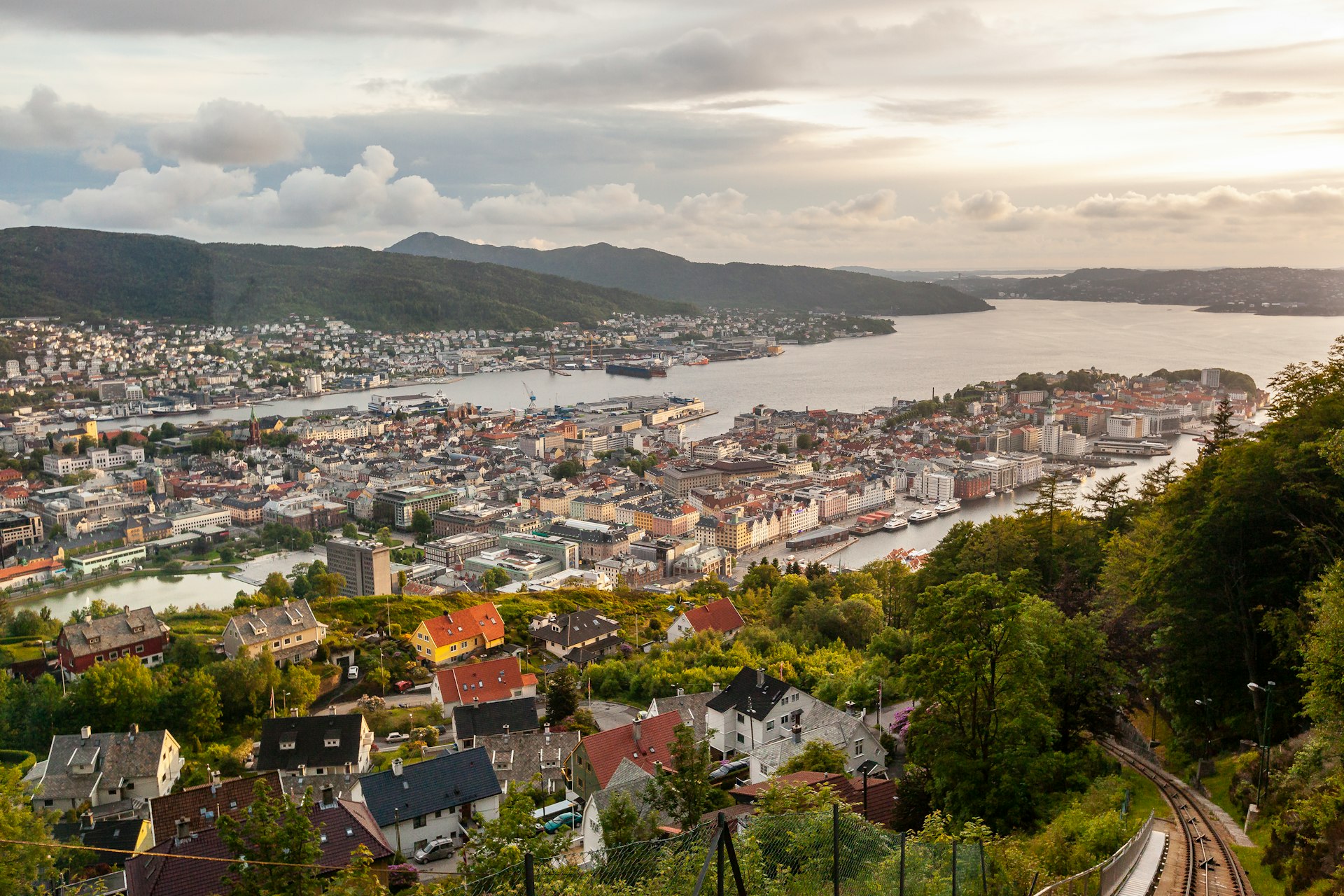 buildings in town facing body of water and mountains under cloudy sky