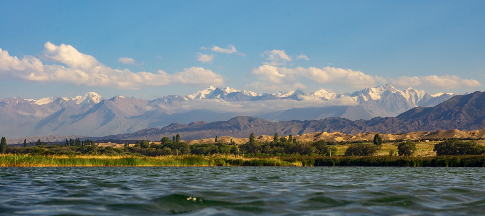 body of water near grass field and mountain at daytime